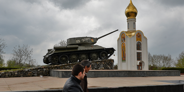 İnsanlar, Nisan 2014'te Moldova'nın Transdinyester'in ana şehri Tiraspol'de, Kızıl Ordu'nun faşist Almanya'ya karşı kazandığı zaferi kutlayan bir anıt olan Sovyet döneminden kalma bir tankın yanından geçiyor.