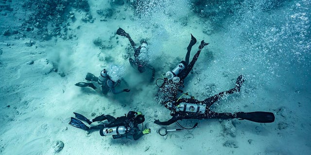 Dalgıçlar, Bahamalar'da bir gemi enkazının bulunduğu yer olan denizin dibine gömülü hazineyi ararken gösteriliyor.