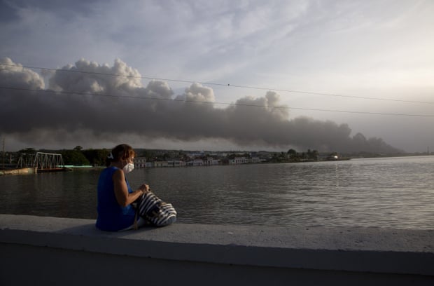 Yangından arka planda duman yükselirken, bir mukim Malecon deniz duvarında oturuyor.